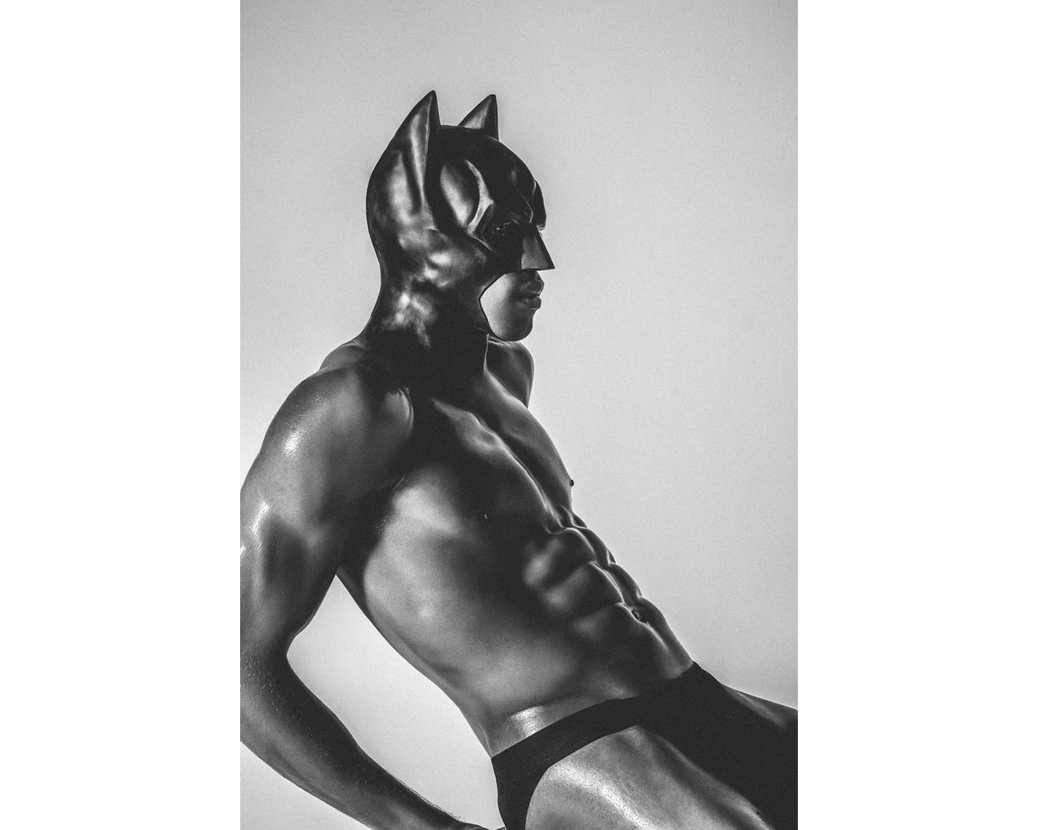 A muscular figure in a black Batman mask, posed dramatically against a plain backdrop, emphasizing his physique in a monochrome style.