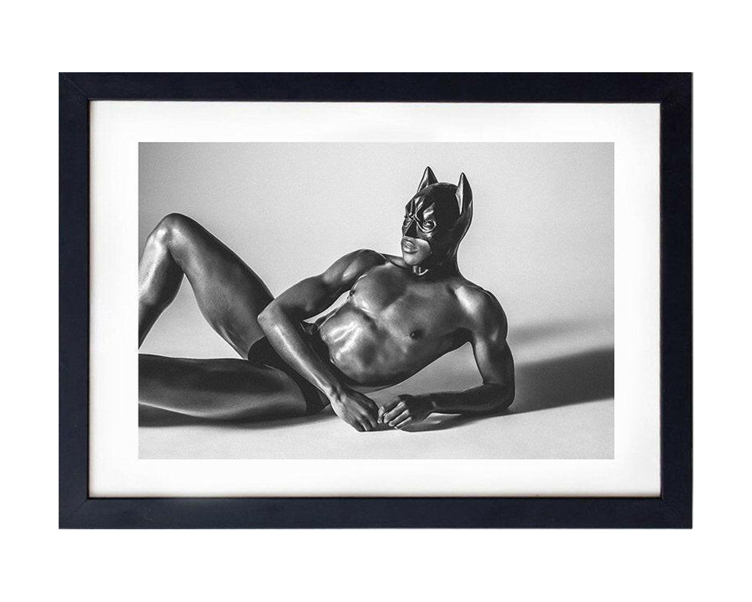 Framed photo of a muscular figure in a sleek black mask reclines against a light background, showcasing a bold and dramatic pose.