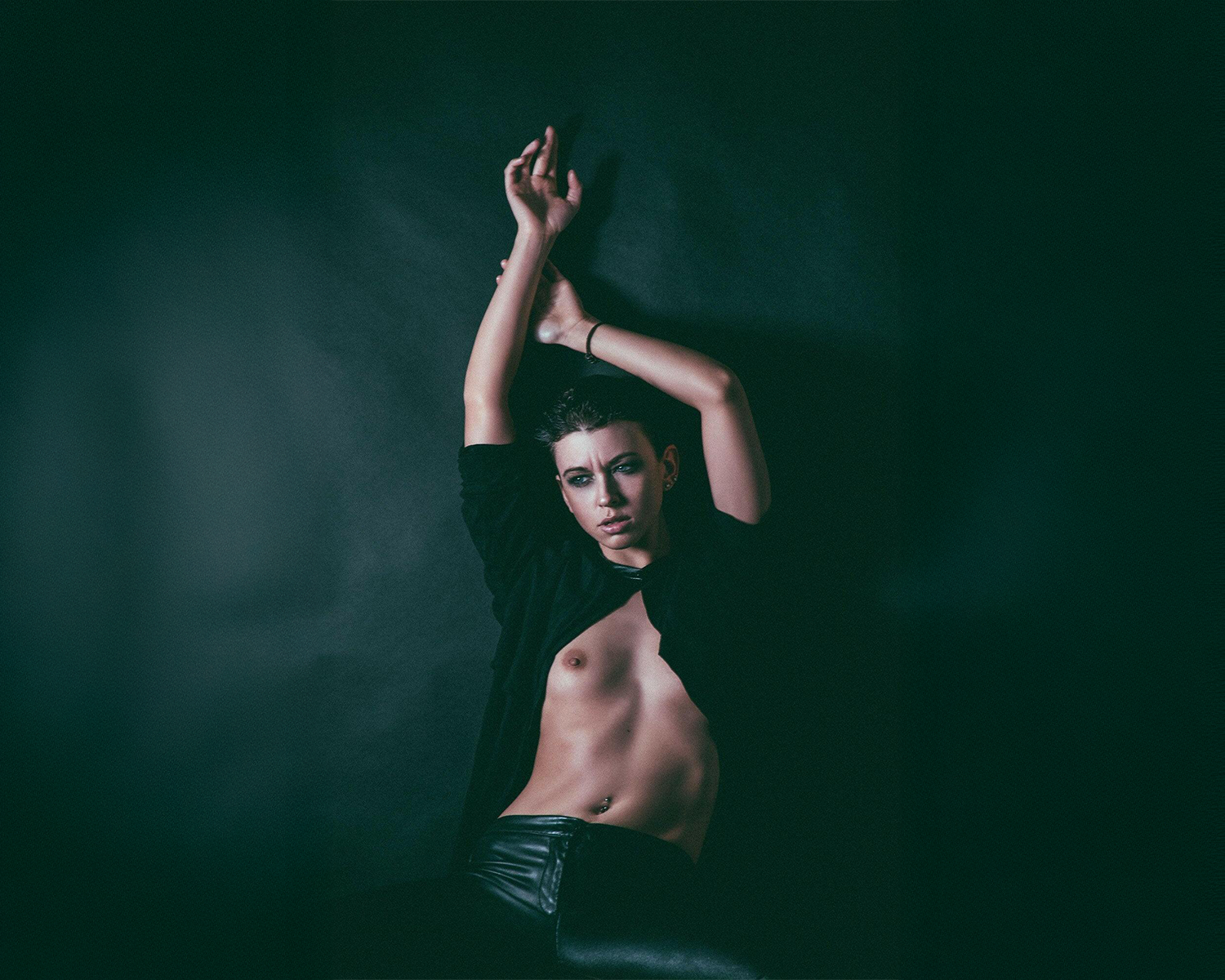 Girl lying on a dark surface with arms raised against a black background