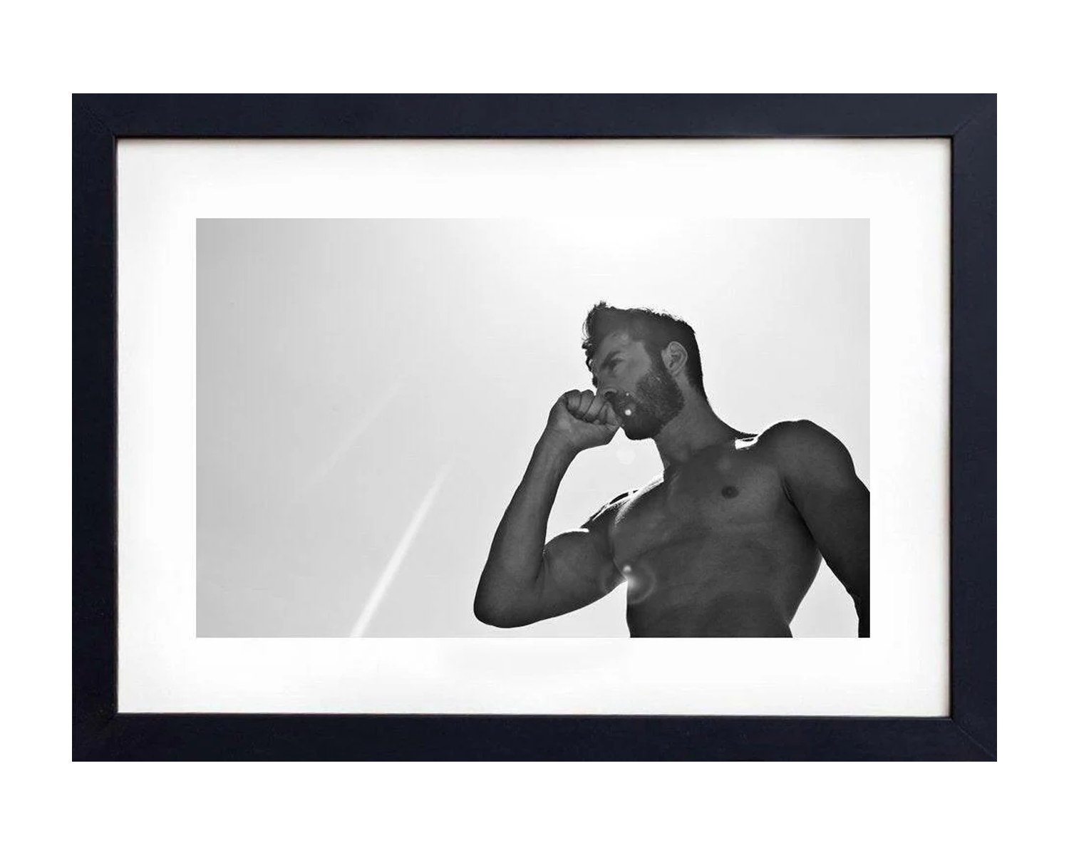Framed black and white photo of A muscular man stands against a bright sky, sipping from a drink with the sun shining overhead in a black and white setting.
