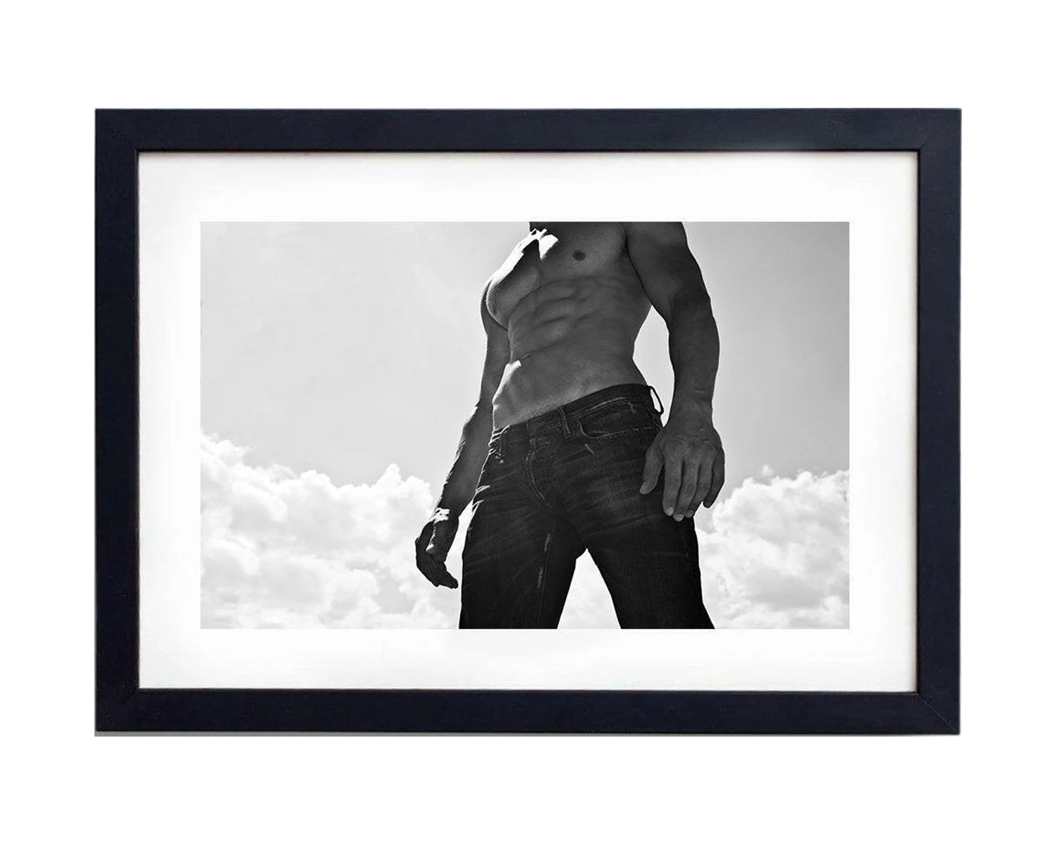 Framed Black-and-white image of a muscular man standing with his torso bare, wearing jeans and striking a strong pose against a cloudy sky.