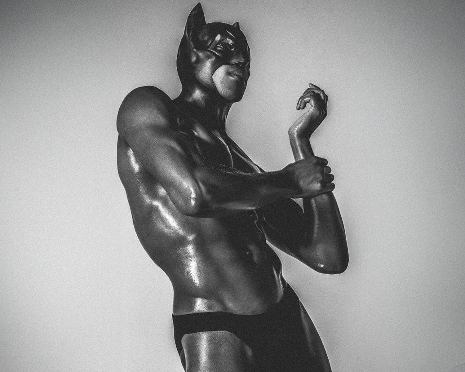 A muscular figure in a black superhero costume striking a pose against a neutral background, exuding a strong and confident vibe.