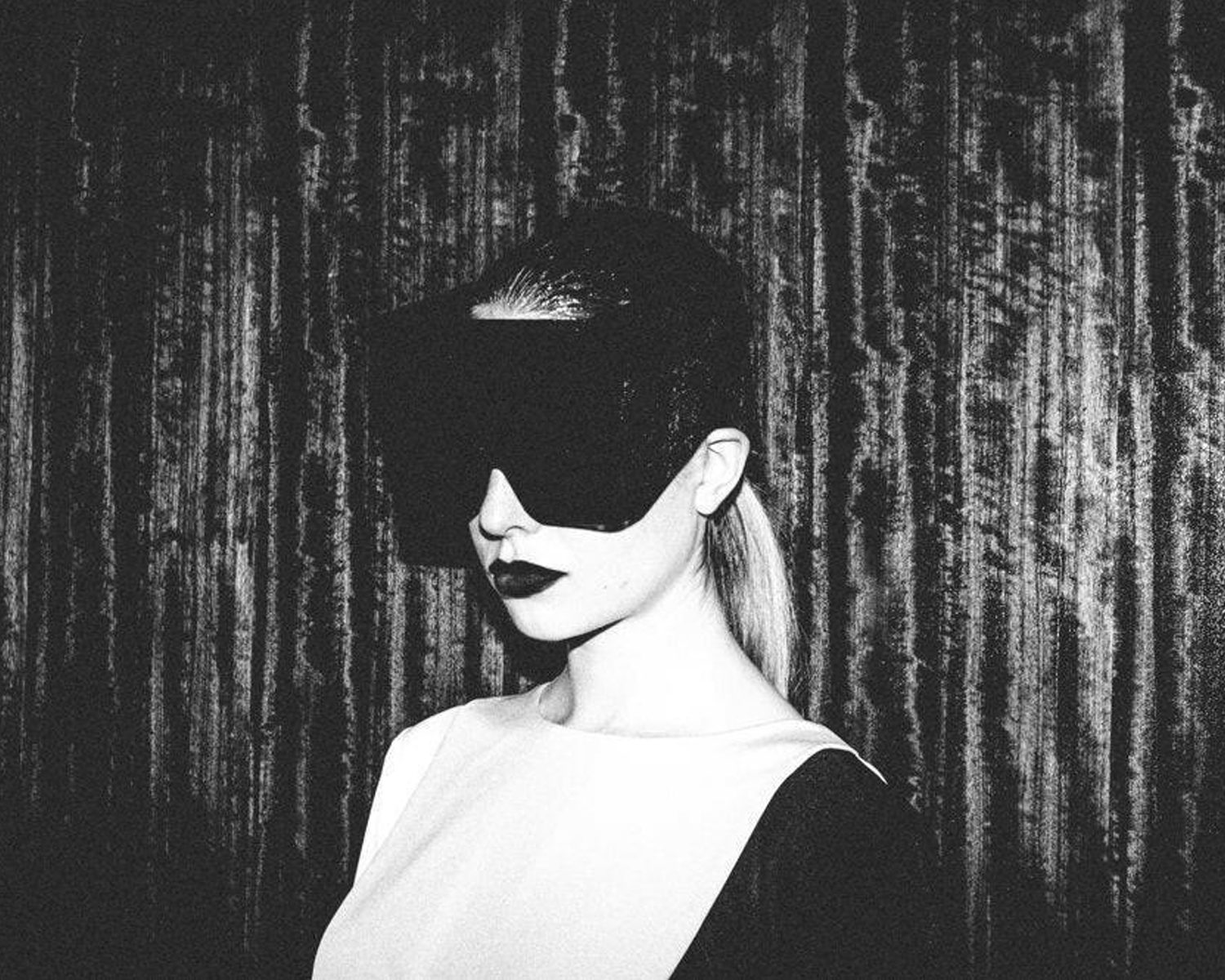 A monochrome image of a figure wearing a futuristic visor, posing against a textured dark background. The atmosphere is mysterious and artistic.