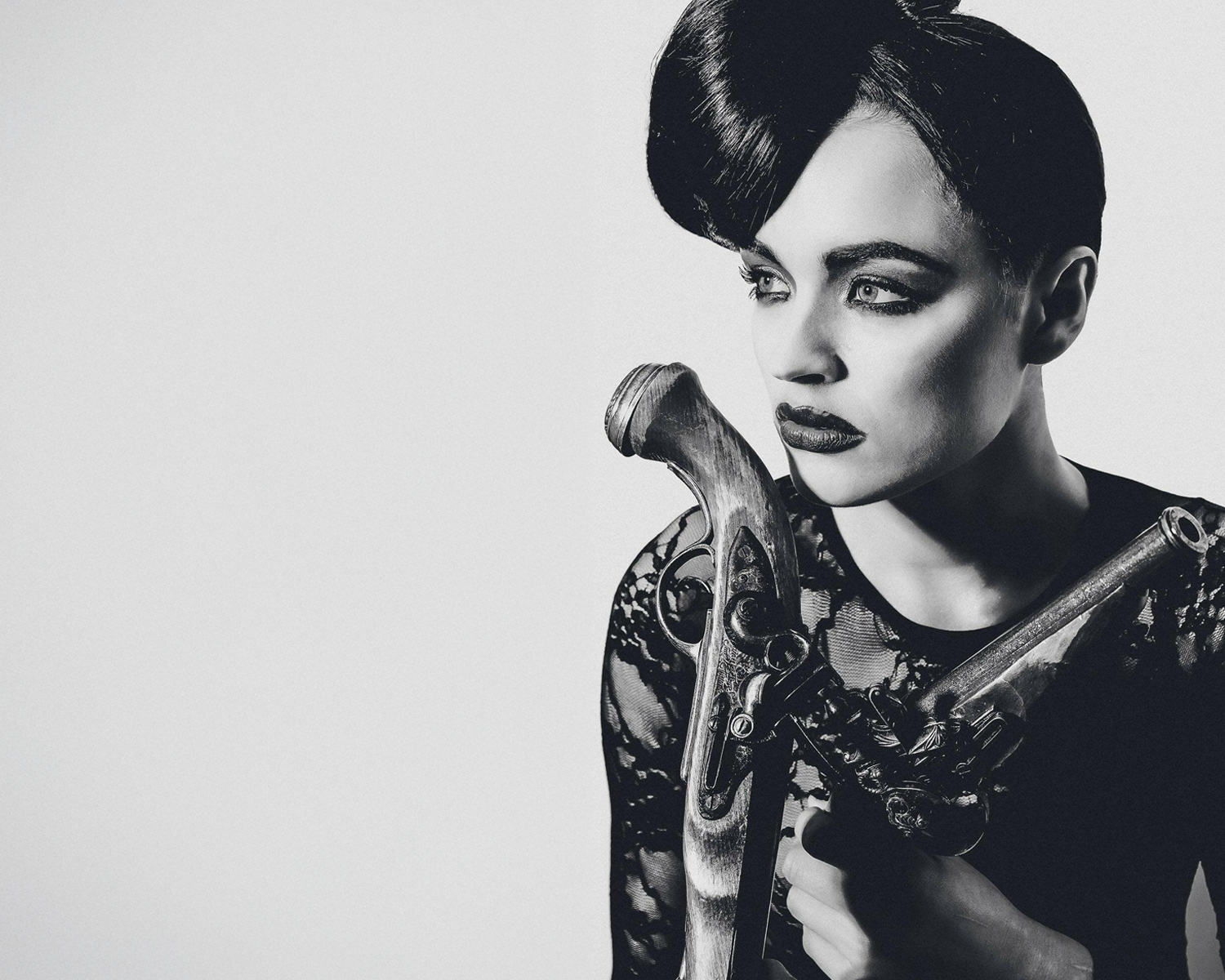 Black and white portrait of a woman holding a vintage-style gun against a plain background