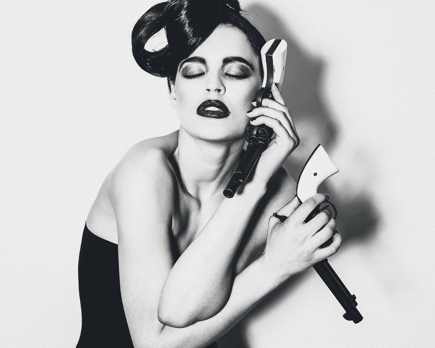 Black and white portrait of a woman holding a gun and a phone, with dramatic lighting.