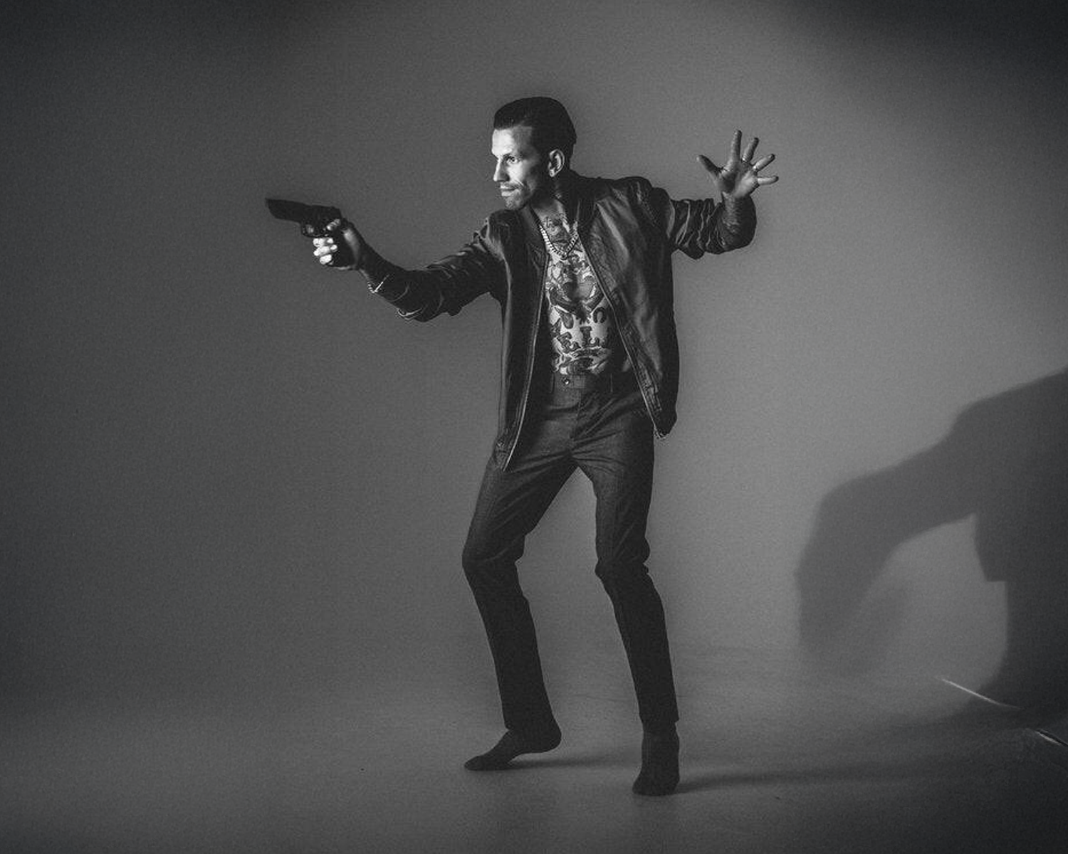 A man dressed in a suit stands with a gun, his shadow creating a dramatic effect behind him.