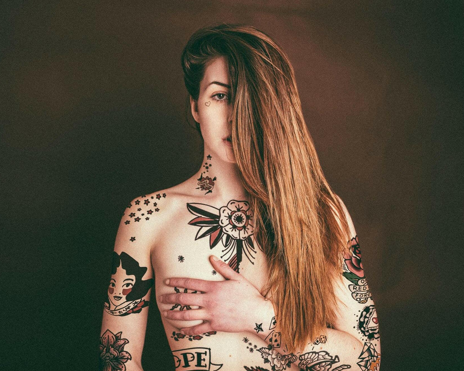 Woman with tattoos on her arms and chest against a dark background