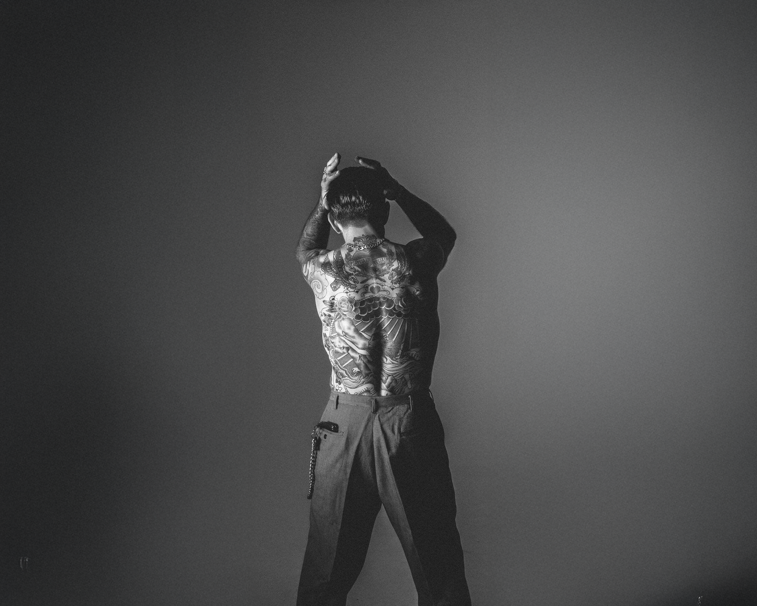 man with a patterned top and dark pants against a plain background