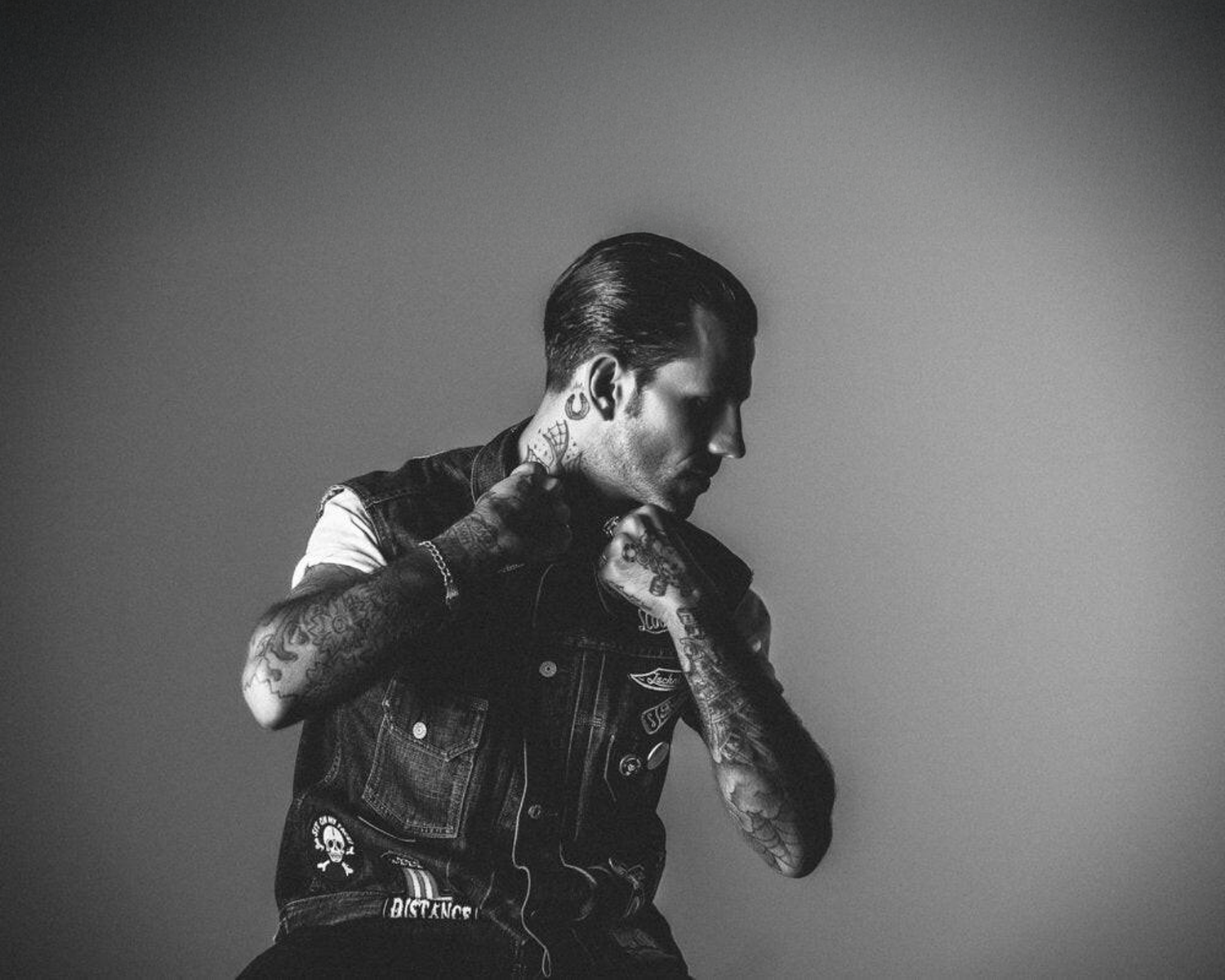 Man with tattoos wearing a denim vest against a plain background