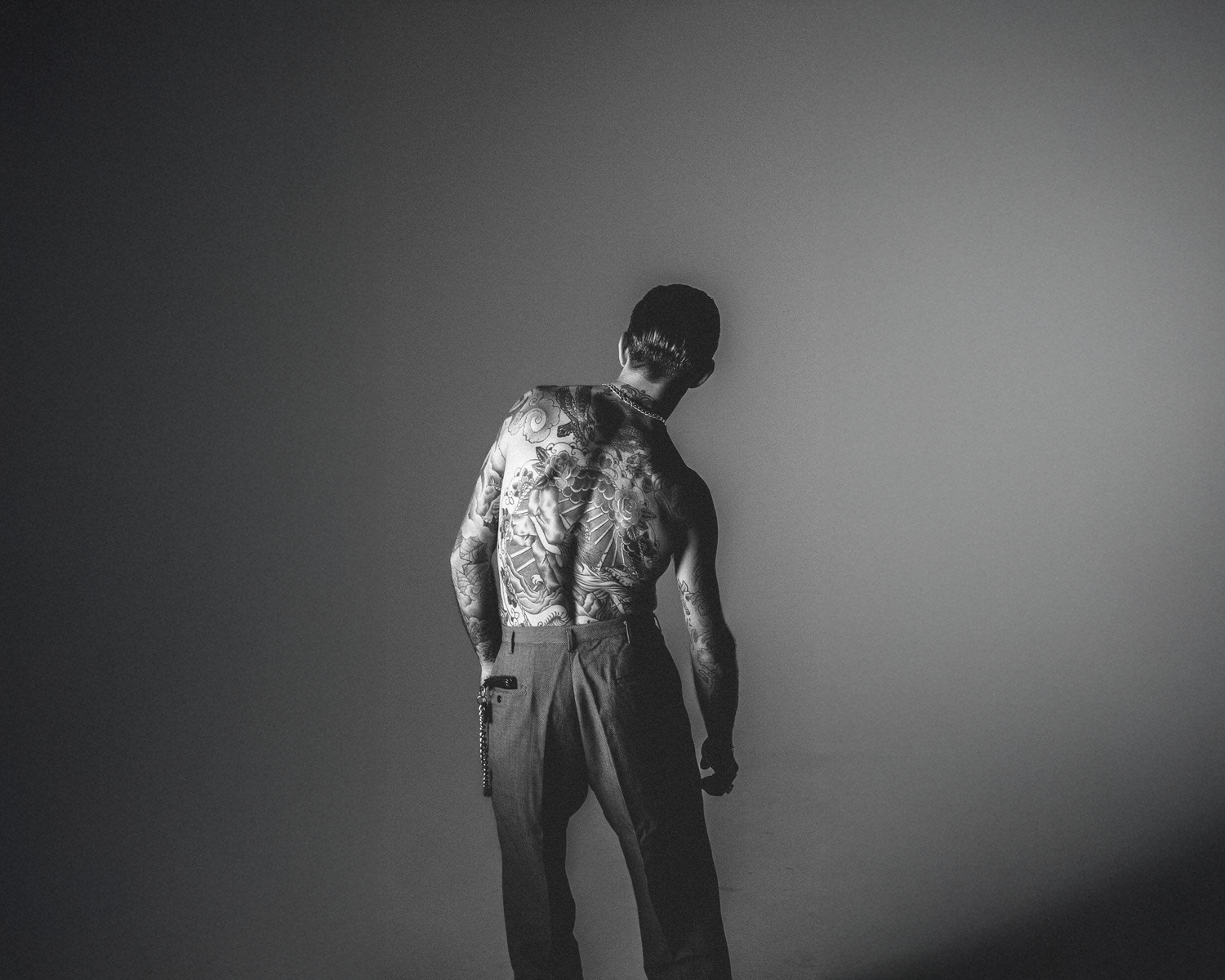 Man with tattoos on his back against a plain wall