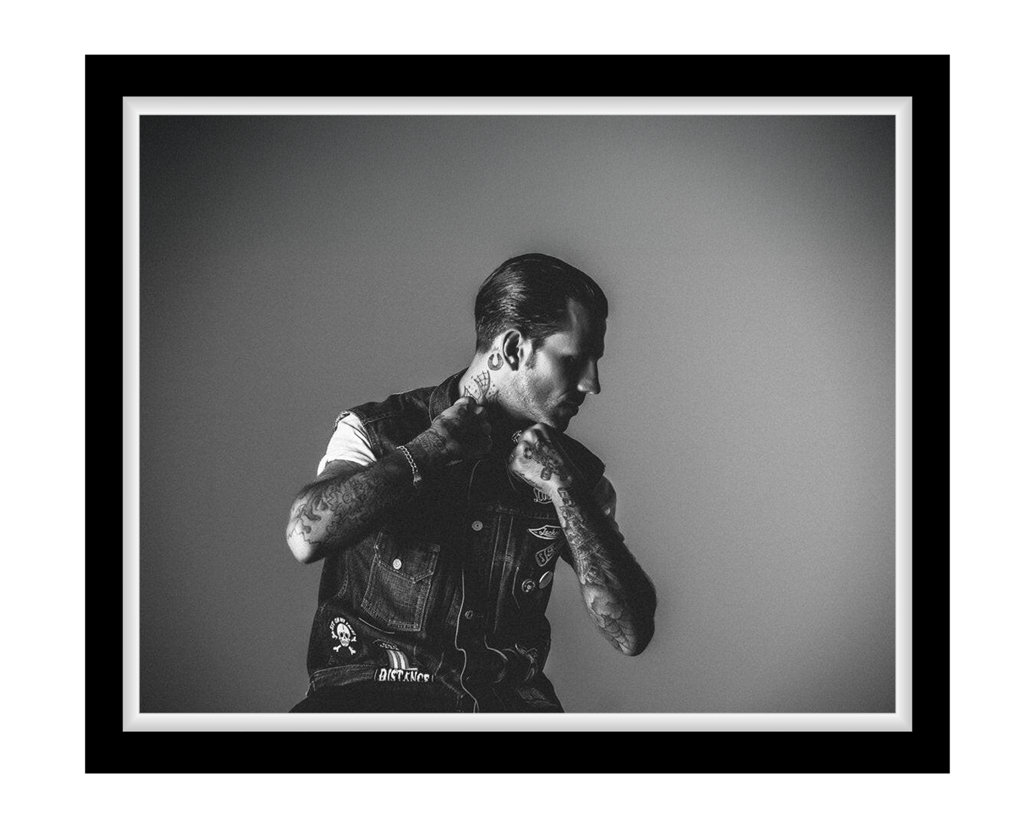 Black and white portrait of a person wearing a denim vest with tattoos on arms, against a plain background.