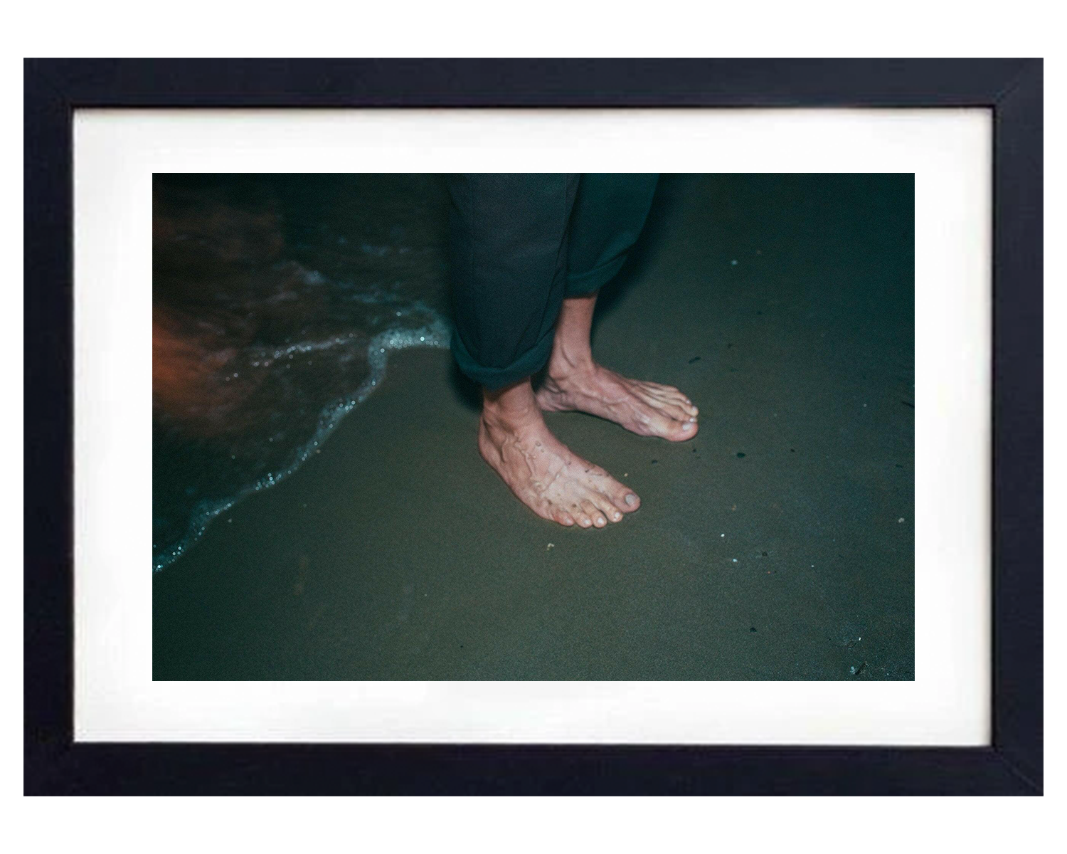 Feet on a beach with waves in the background, framed in black