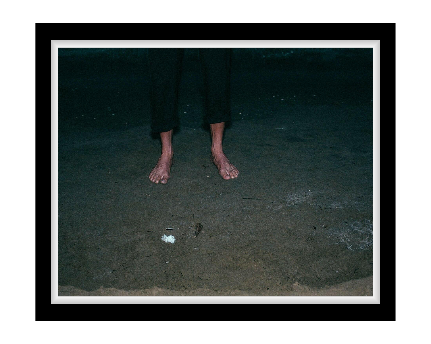 Person standing on a dark sandy beach at night with minimal lighting.