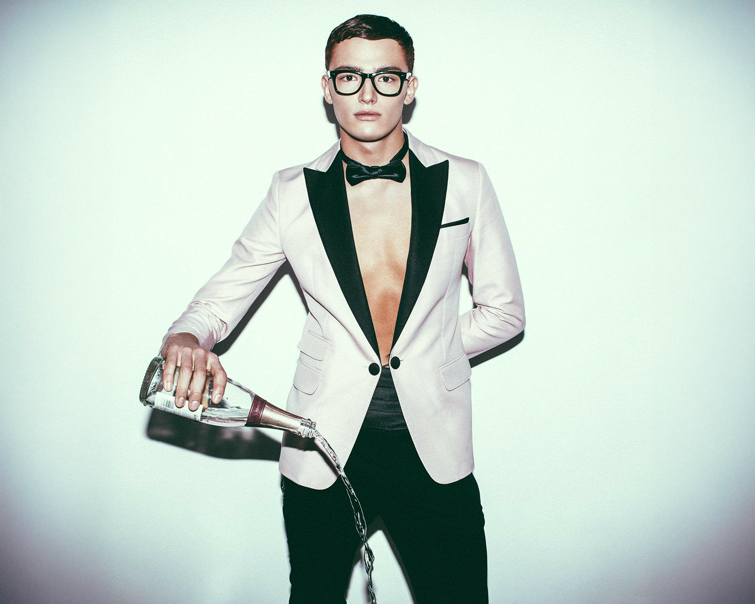 Man in a white tuxedo pouring champagne against a light background