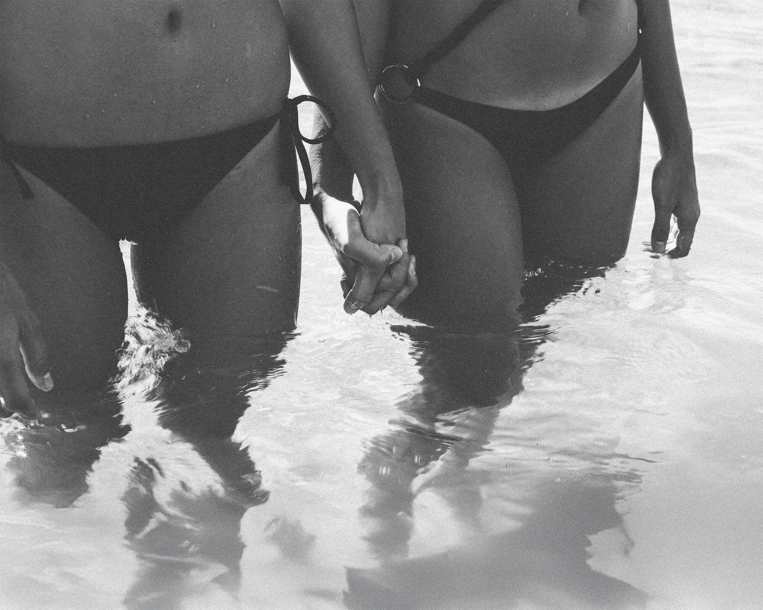 Two people holding hands in shallow water, wearing swimsuits.