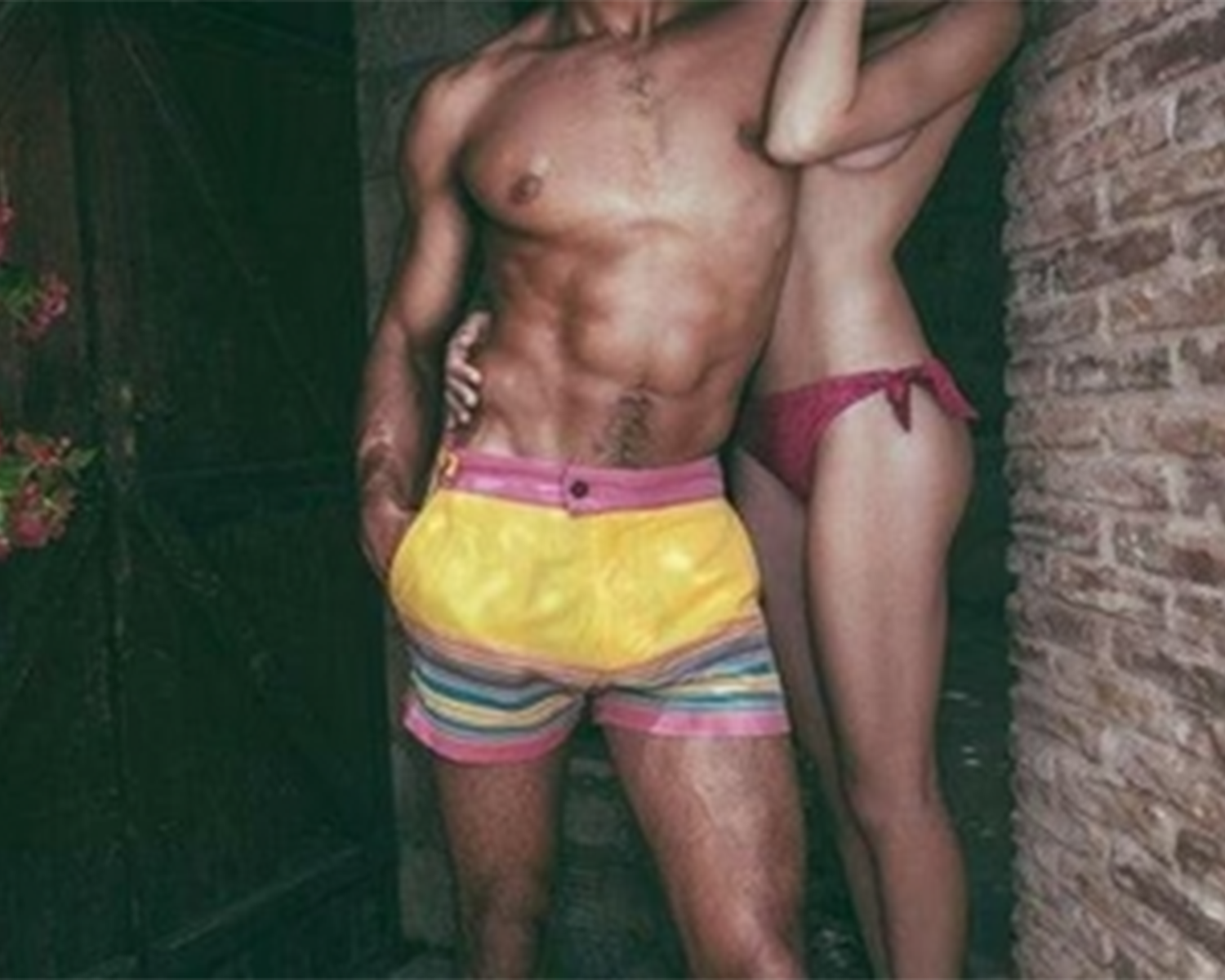 A man and woman in colorful swim trunks, standing side by side and posing for a cheerful photo outdoors.