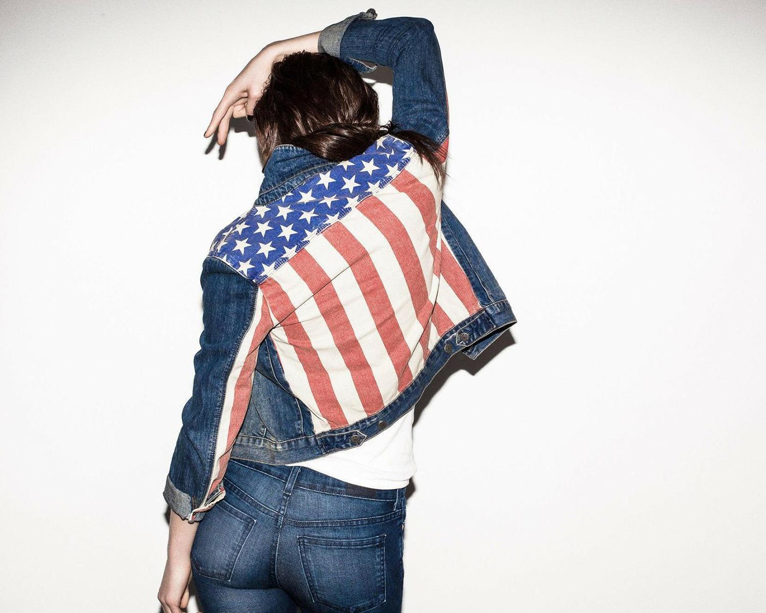 Person wearing a denim jacket with an American flag design on a plain background