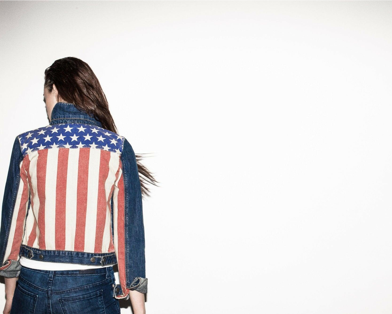 Person wearing a denim jacket with an American flag design on a white background