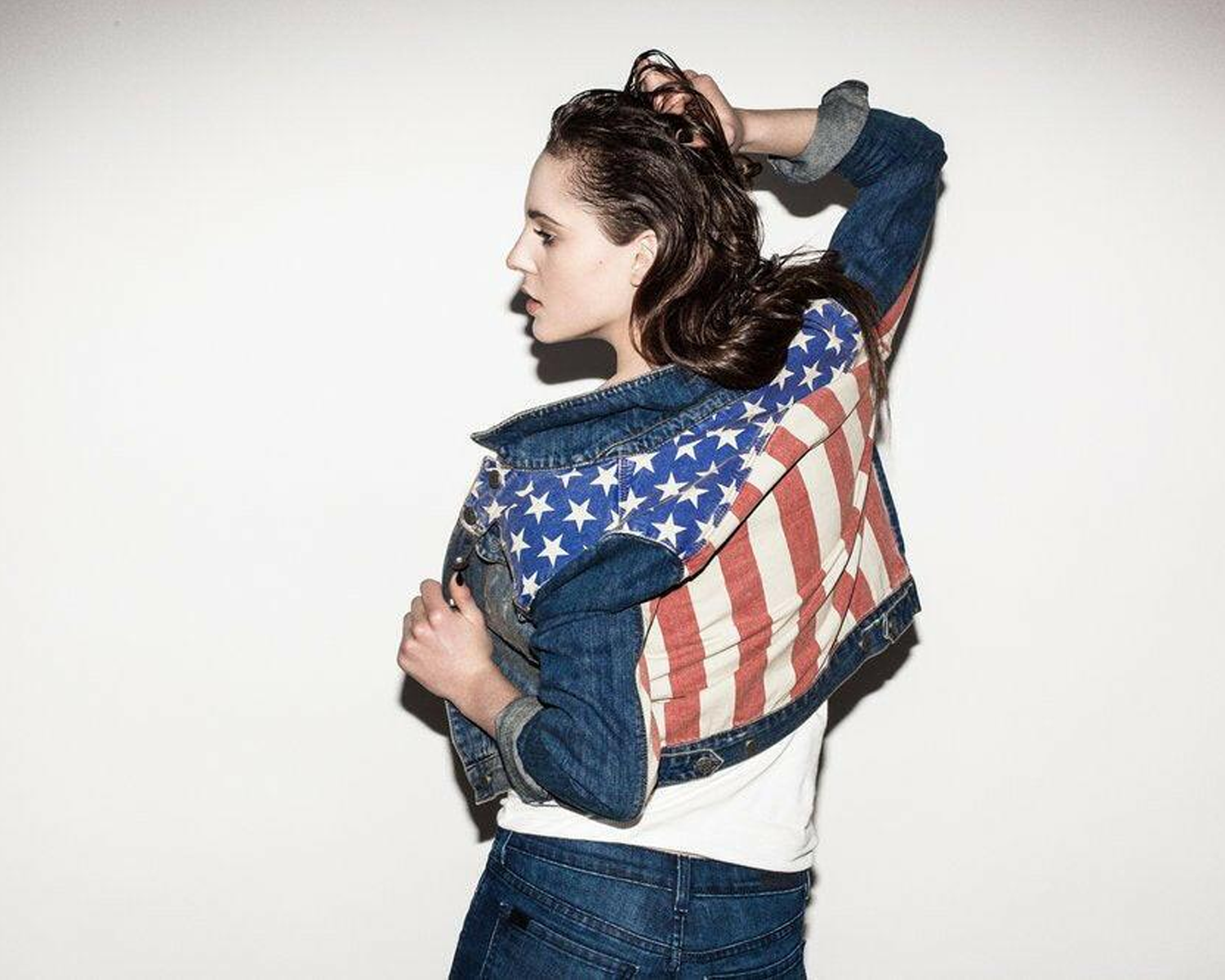 Person wearing a denim jacket with an American flag pattern on a white background
