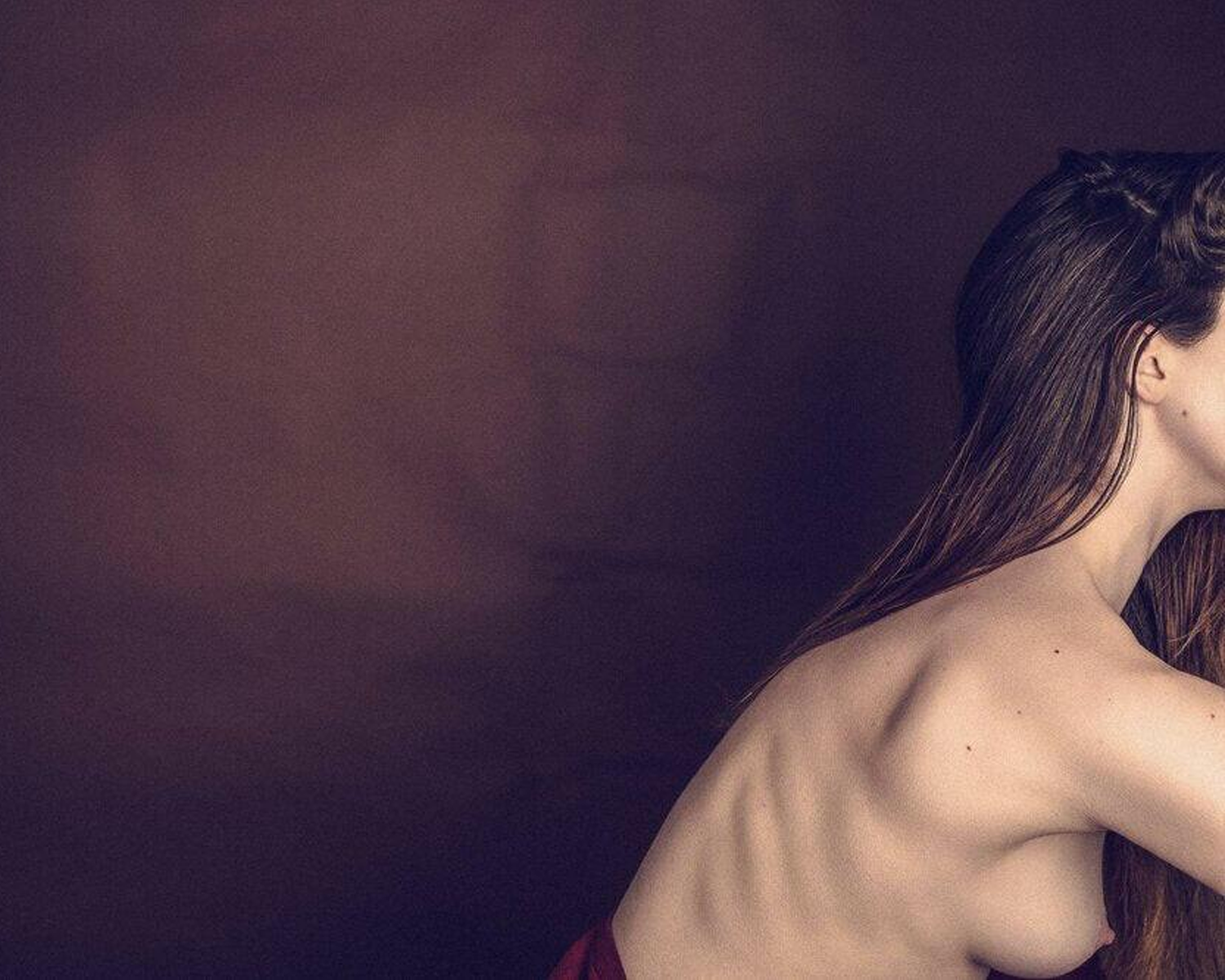 A side profile of a woman with long hair, partially bare, against a soft brown background, showcasing elegant posture.