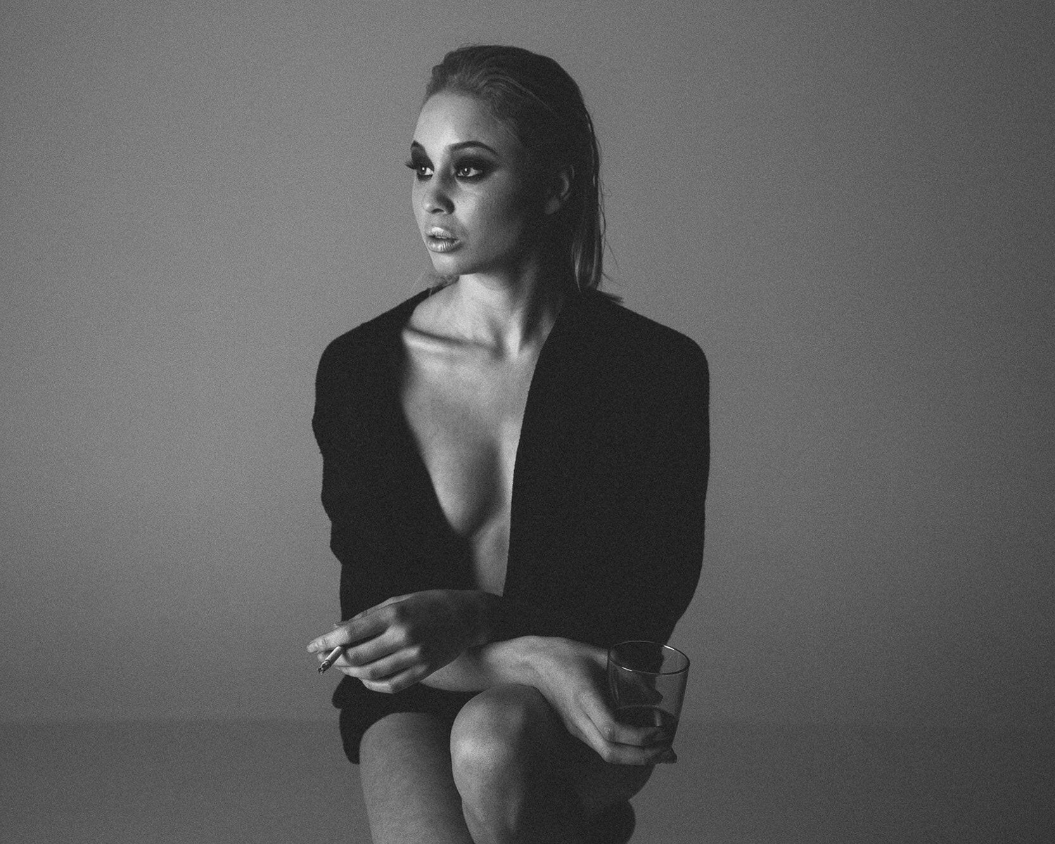 A woman seated on a chair, casually holding a cigarette, with a thoughtful expression.